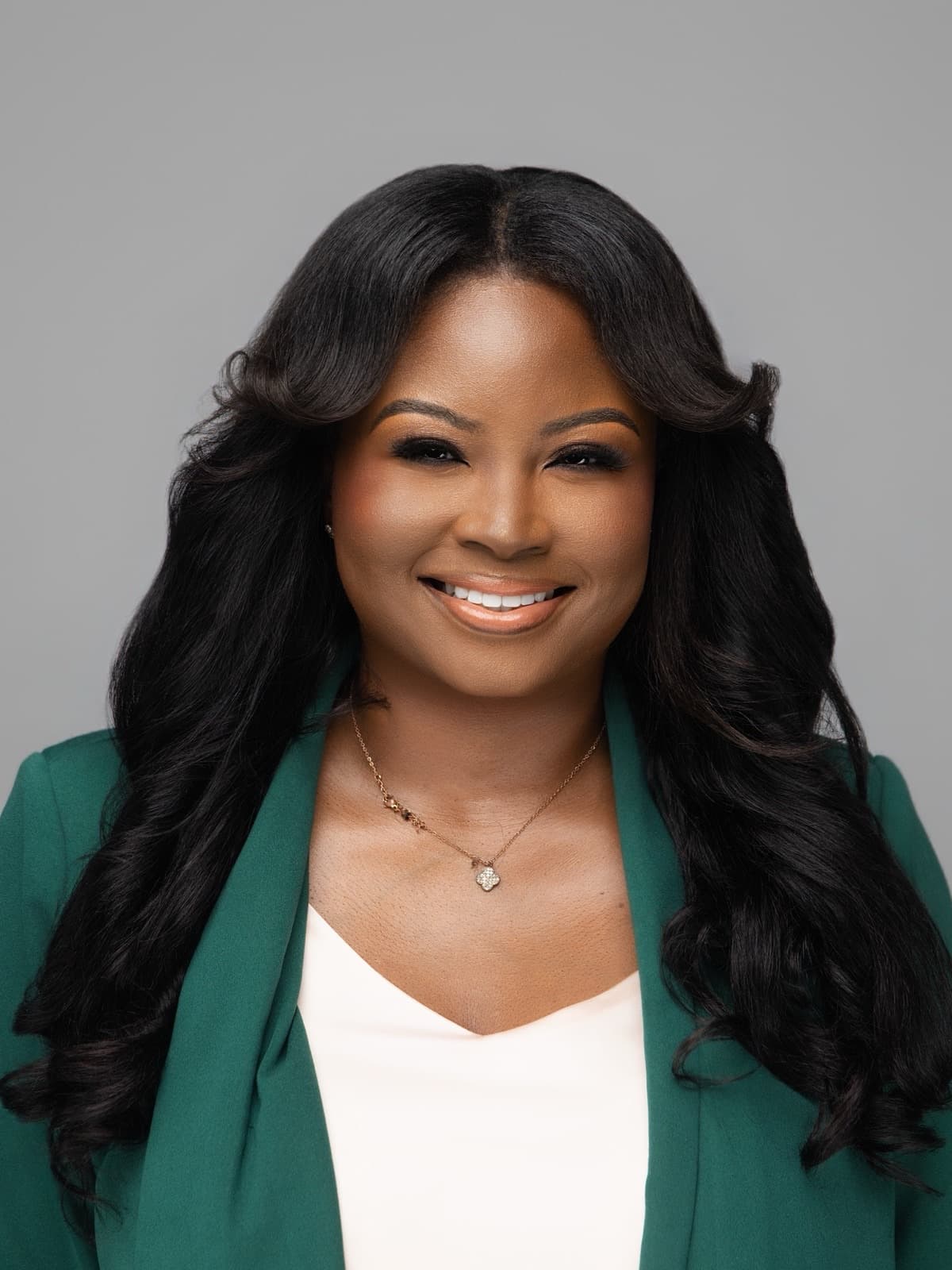 Patricia, founder and creative director of Soleil Signature Experiences, in a green blazer against a soft grey background